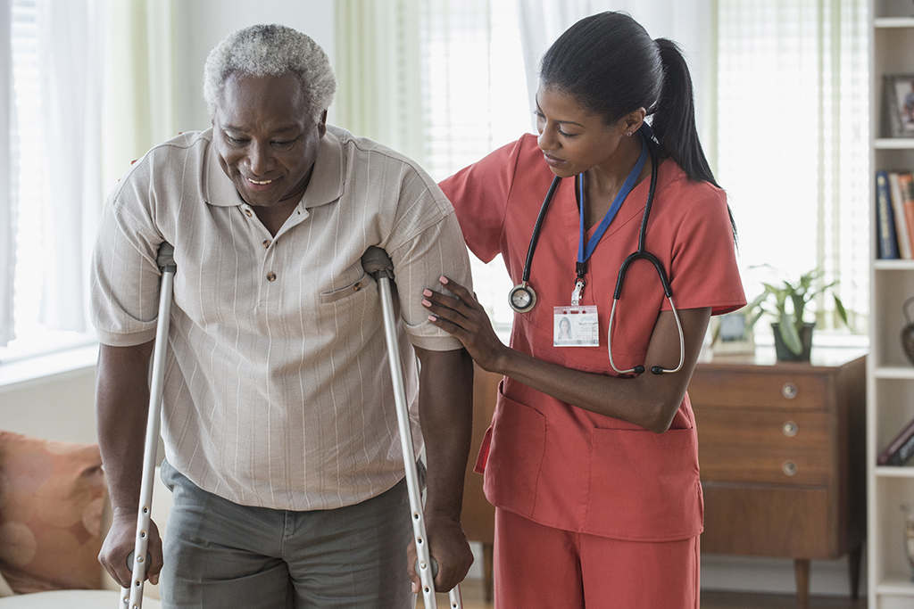 Caregiver helping older man walk on crutches