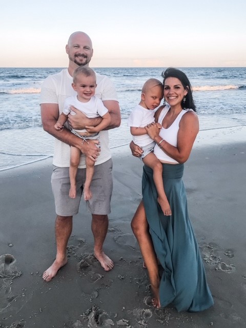 The Berry family is standing together at the beach and the ocean is behind them.