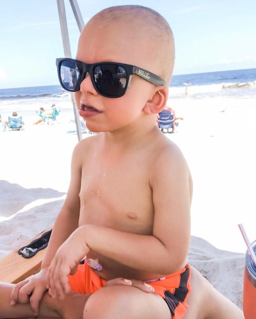 Little Nolan is enjoying playing at the beach while wearing sunglasses.