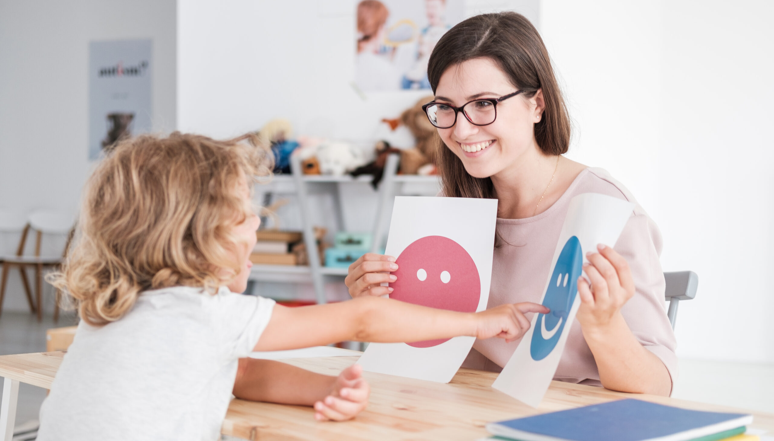 Smiling counselor holding pictures during meeting with young patient with autism