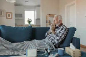 A elder guy sitting on sofa sneezing