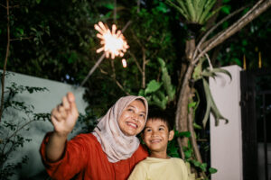 Beautiful young hijab mother and son, playing sparkler, in garden at home, celebrating fourth of july