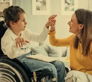 Young girl in a wheelchair smiling and interacting with a caregiver at home.