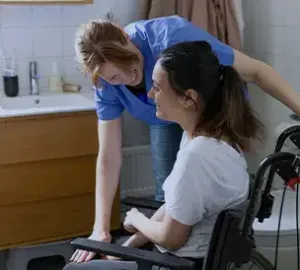 Caregiver assisting a woman in a wheelchair with daily activities in a home bathroom.