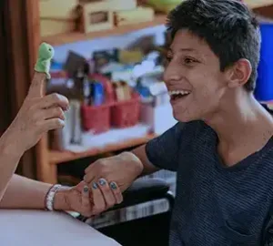 Caregiver engaging a smiling young man with a playful finger puppet during therapy.