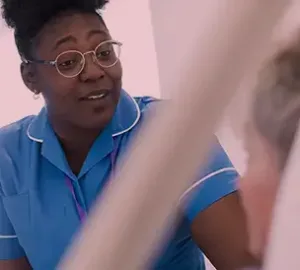 Nurse in blue uniform attentively speaking to a patient in a clinical setting.