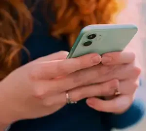 person holding a mint green smartphone and texting, close-up view of hands with long red hair in the background