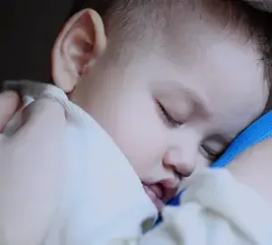sleeping baby resting peacefully on an adult's shoulder, dressed in light clothing