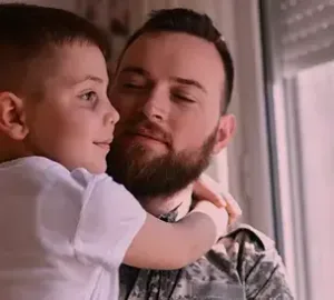 man in military uniform holding his child close, sharing an affectionate moment by the window