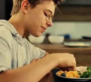 young boy enjoying a meal, eating scrambled eggs and salad while seated at a table indoors
