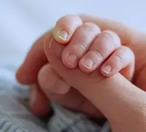 Close-up of a small child’s hand holding onto an adult’s finger, symbolizing care and support.