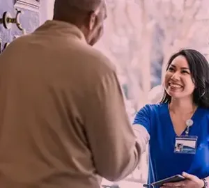 Smiling healthcare worker shaking hands with a man at a doorway, showcasing in-home care service.